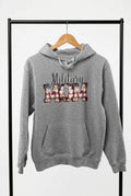 A heather gray pullover hoodie hanging on a wooden hanger against a black wire grid display wall. The hoodie features a front graphic that reads 'Military Mom' with 'MOM' filled with a red, white, and blue striped pattern resembling the US flag.