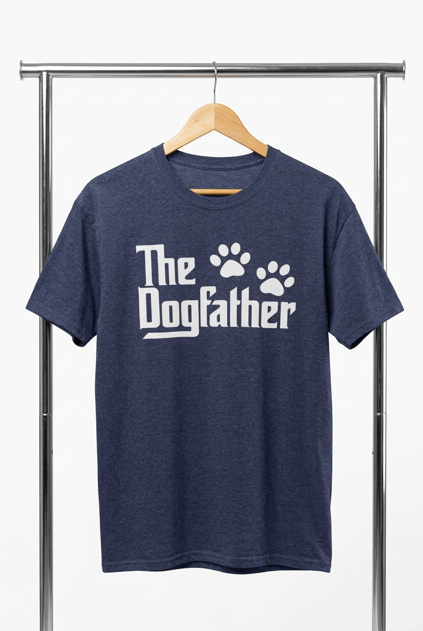 A navy blue heather crewneck t-shirt hanging on a wooden hanger against a black wire grid wall. The shirt features the text 'The Dogfather' in a white stylized font, with two white paw prints replacing the letter 'o' in 'Dog'.