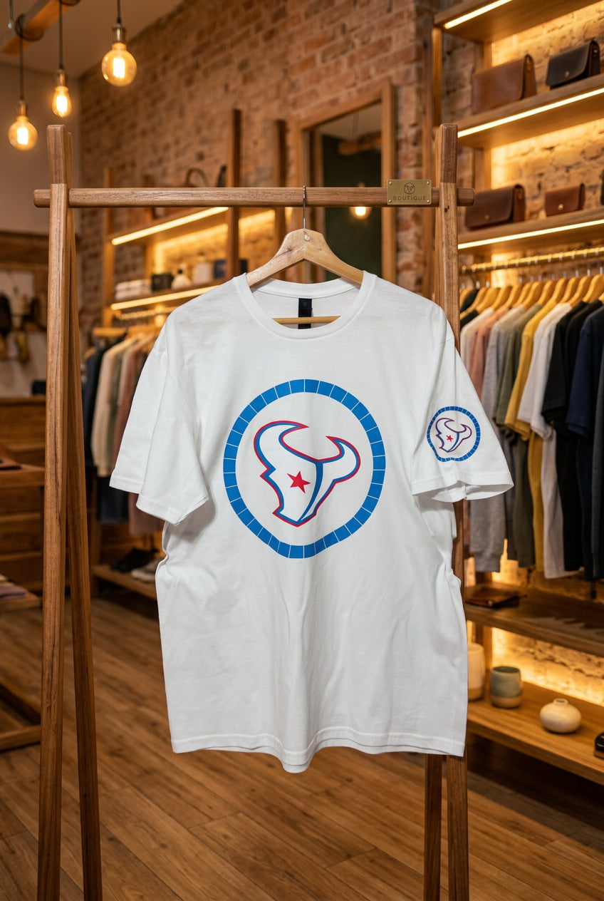 A white short-sleeve t-shirt hanging on a wooden hanger against a black wire grid wall. The shirt features a large circular graphic on the front with a blue segmented border, a stylized red and blue bull head logo, and a small matching logo on the left sleeve.