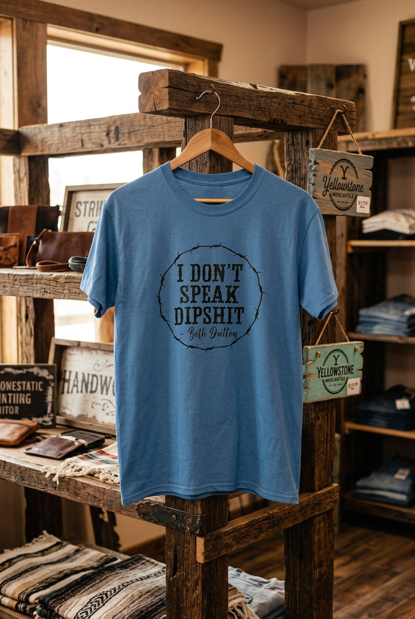 A blue short-sleeve graphic t-shirt hanging on a wooden hanger against a black wire grid display wall. The shirt features a circular black graphic print on the chest that reads 'I DON'T SPEAK DIPSHIT' with 'Gabe Guitars' written below.