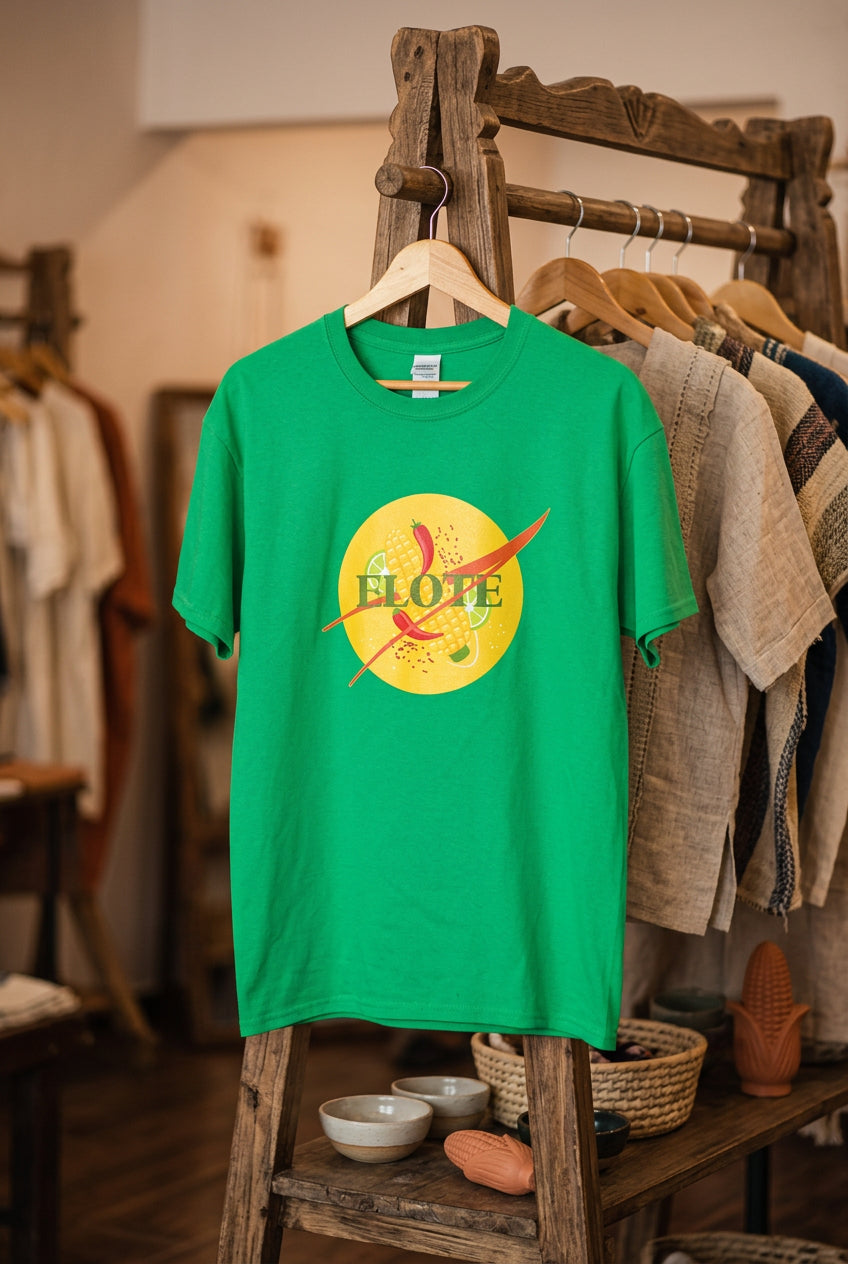 A bright green short-sleeve t-shirt hanging on a wooden hanger against a black wire grid wall. The shirt features a large yellow circular graphic on the chest with a red chili pepper and the word 'ELOPE' written across it.
