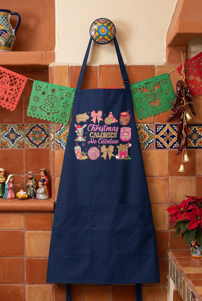 A navy blue apron with front pockets and a colorful graphic print reading 'Christmas Calories No Cuentan' surrounded by festive illustrations, displayed on a mannequin torso over a light gray long-sleeve shirt against a white paneled background.