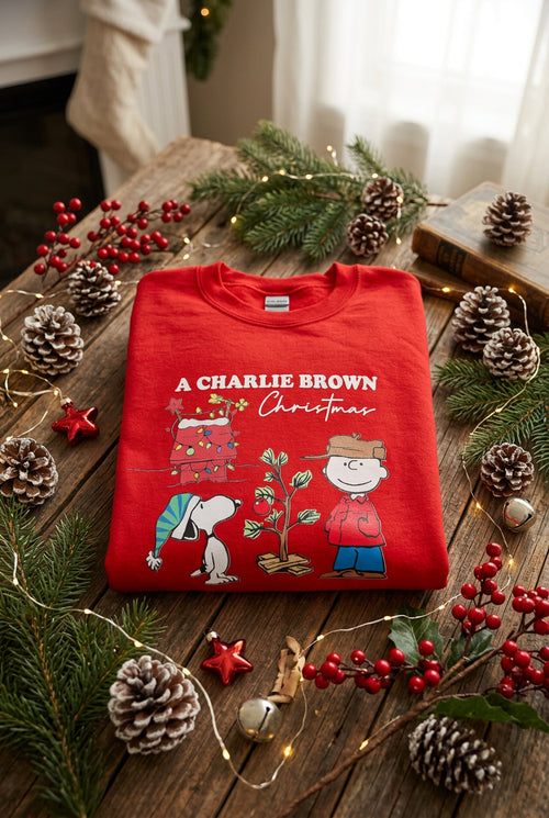 A folded red crewneck sweatshirt featuring a 'Christmas' graphic print with boy and his dog on a white background.