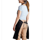 A woman shown from the back wearing a black bib apron tied around her waist over a light blue t-shirt and tan pants, against a plain white background.