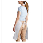 A woman shown from the back wearing a light gray kitchen apron tied around her waist over a light blue t-shirt and tan pants, against a plain white background.