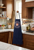 A navy blue apron with a Houston baseball logo printed on the chest, displayed on a knob in a kitchen