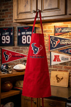 A bright red apron with a Houston football logo and text, displayed on a knob in sports themed room.