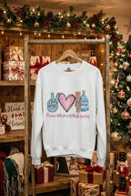 An off-white crewneck sweatshirt displayed on a mannequin torso with blue jeans. The sweatshirt features a colorful graphic of a peace sign, a pink heart, a nutcracker, a Christmas tree, and the text 'Peace Love Nutcracker'.