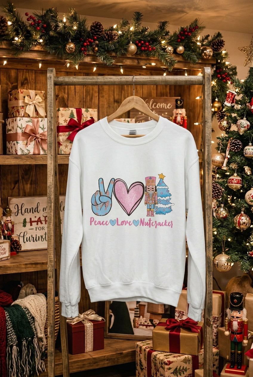 An off-white crewneck sweatshirt displayed on a mannequin torso with blue jeans. The sweatshirt features a colorful graphic of a peace sign, a pink heart, a nutcracker, a Christmas tree, and the text 'Peace Love Nutcracker'.